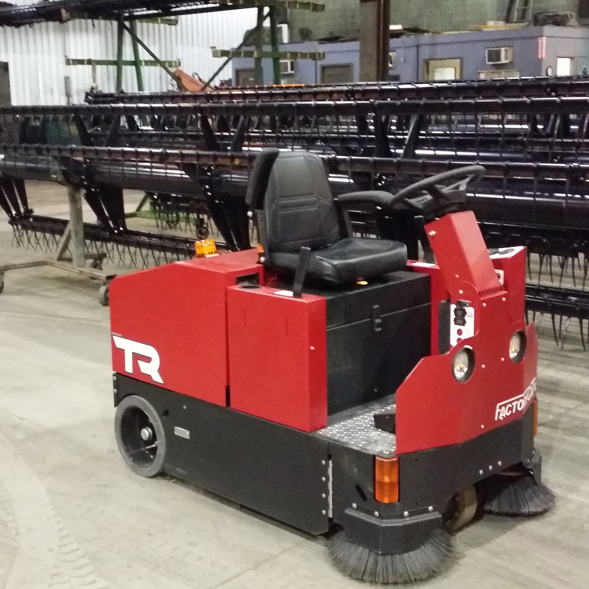 The Red Factory Cat TR Rider is cleaning an industrial floor